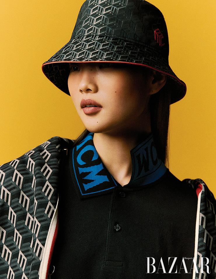 피케 로고 폴로 셔츠, 어깨에 걸친 트랙 재킷, 모노그램 자카드 버킷 모자는 모두 MCM.