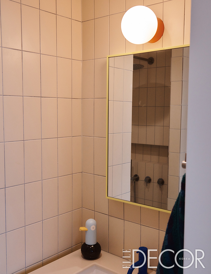 파란색 볼라(Vola) 수전과 노란 프레임의 붙박이 거울, 주황색의 월 램프가 어우러진 욕실.