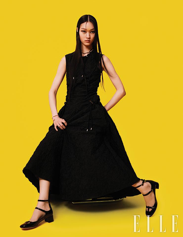 스트링 장식의 블랙 슬리브리스 드레스와 블랙 볼형 초커, 로고 디테일 뱅글, 진주 장식 뱅글, 앵클 스트랩 메리 제인 슈즈는 모두 Dior.